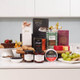 Gourmet Goodies Gift Box. A variety of gourmet food items displayed on a white countertop. There are cakes, cookies, jars of jams. Packaging includes colorful boxes and labels for different treats, creating an inviting arrangement. Gourmet Goodies Gift Box. A variety of gourmet food items displayed on a white countertop. There are cakes, cookies, jars of jams. Packaging includes colorful boxes and labels for different treats, creating an inviting arrangement.